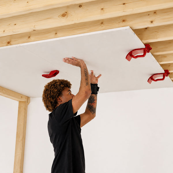Installer using Board Aid to support a ceiling plasterboard sheet during one-person plasterboard and drywall installation.